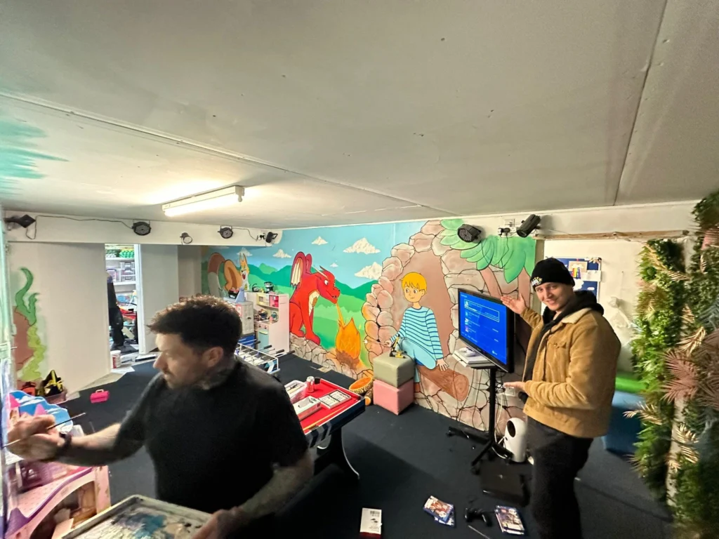 Team members working inside the Your Love Rara community hub featuring wall murals of a red dragon and a character.