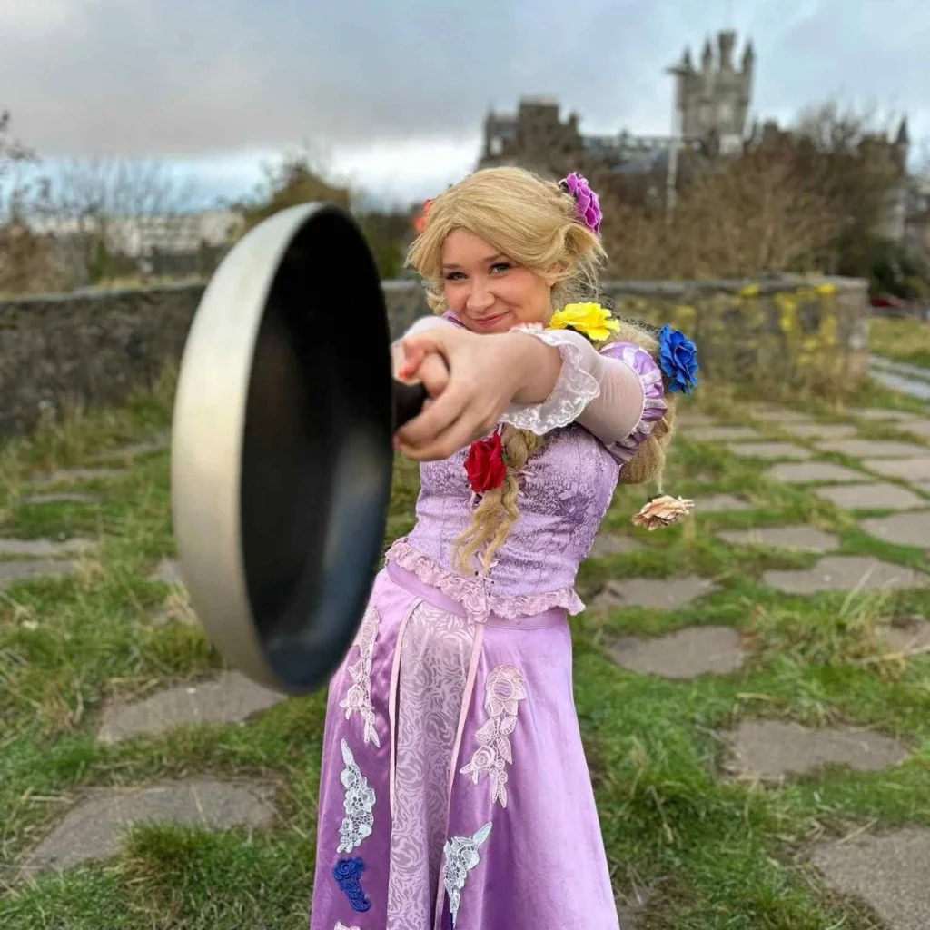 A performer dressed as a tower princess with long hair holding a frying pan at a Your Love Rara themed children's party.