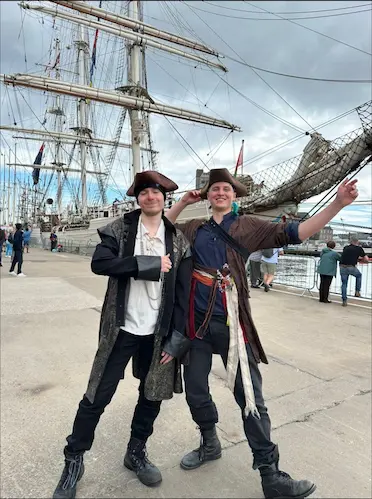 Two Your Love Rara performers dressed in high-quality pirate costumes standing in front of the Tall Ships at Aberdeen Harbour.